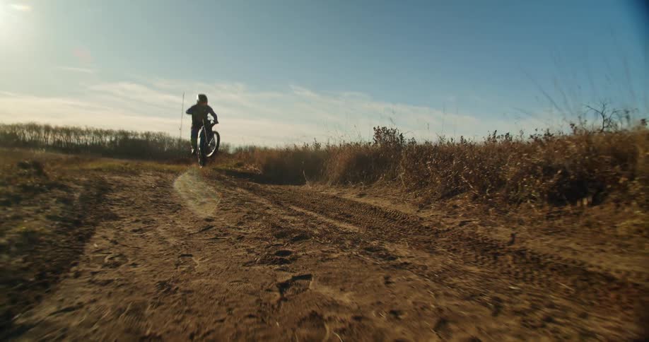 Rider does a wheelie on a dirt bike along a rural trail under a clear sky