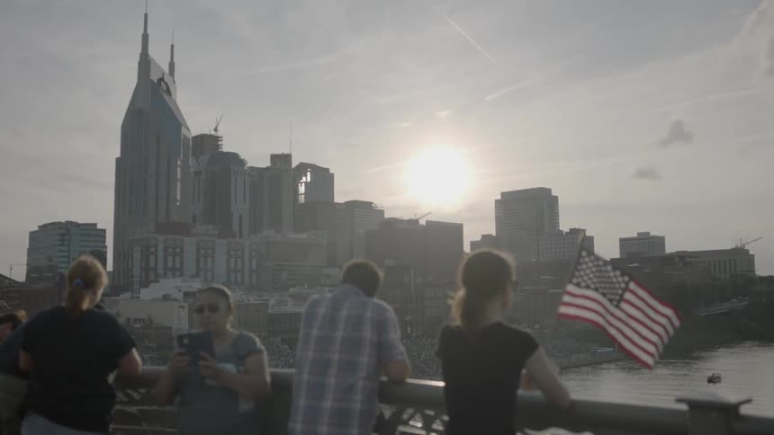 A woman holds an american flag by a railing near water