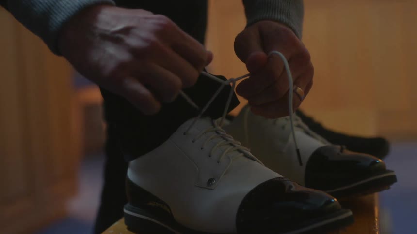 A man ties his black and white shoes