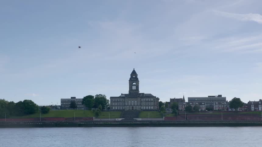 A bird flies over a body of water with buildings in the background