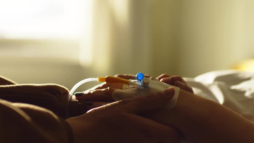 Person holding hands of a patient lying in a hospital room