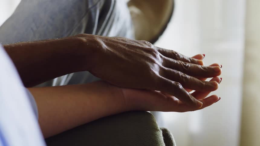 Two people tenderly hold hands while sitting close together conveying a sense of emotional intimacy