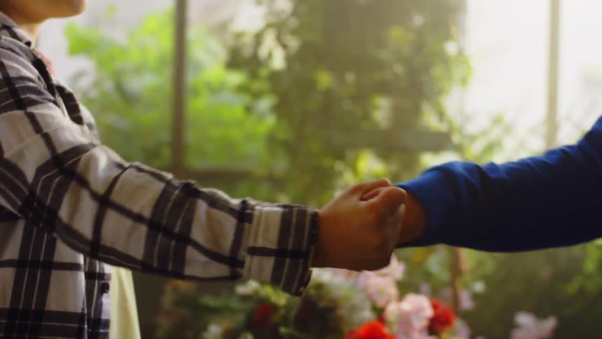 Two kids do a handshake with a fist bump inside a building filled with flowers at midday