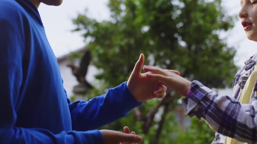 Two male teenagers play rock paper scissors while standing outdoors during daytime