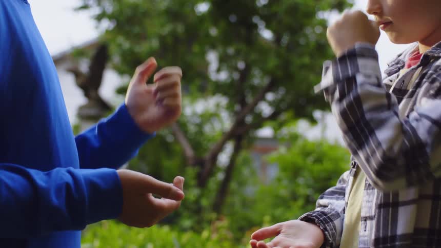 Two kids are playing rockpaperscissors outdoors caught midaction during the game
