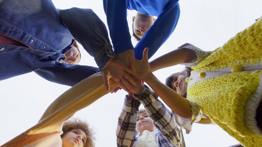 A group of kids stands in a circle with their hands stacked together seen from a lowangle shot looking up