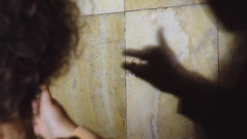 Child doing a hand shadow puppet of a dog on a tile wall