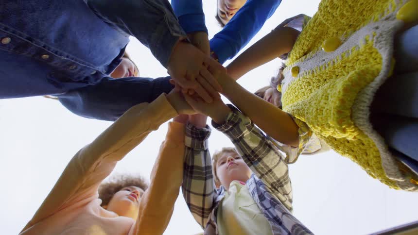 Group of children standing in a circle outdoors during daytime outstretch their arms in the centre and raise them in the air in celebration
