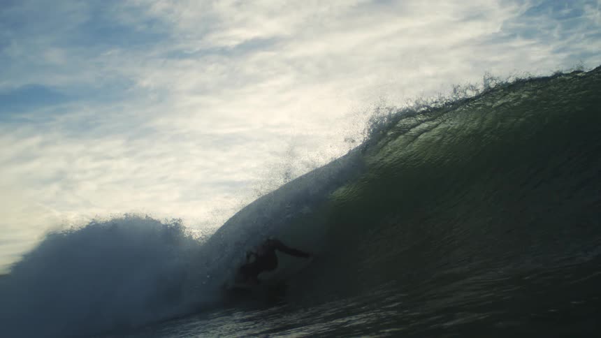 A surfer is riding inside a large curling wave under a cloudy sky