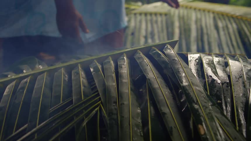 A person is smoking large green palm leaves while handling them outdoors