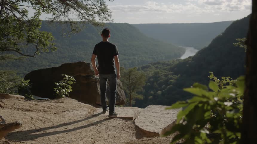 A man walks toward a ledge that overlooks a mountain valley