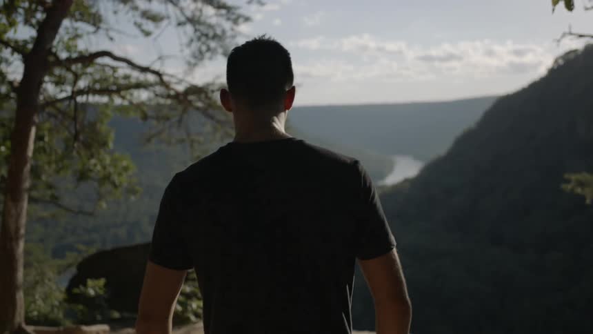 A man walks toward a ledge that overlooks a mountain valley