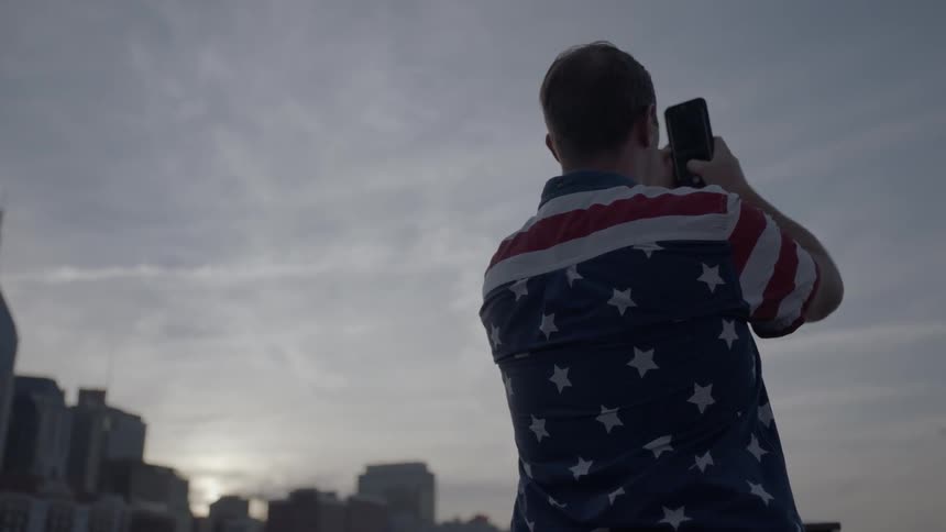 Man in a flag shirt records a cloudy sky
