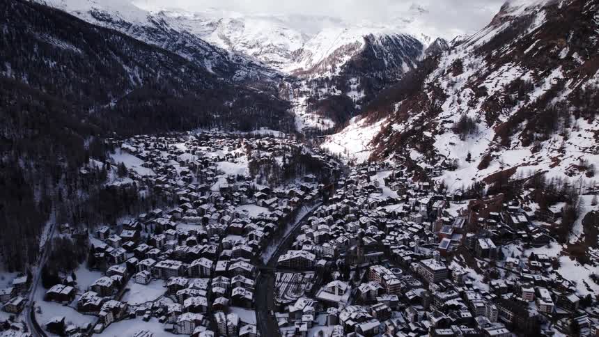 A city nestled among mountains blanketed in snow from the winter season with the midday sun casting a soft glow over the landscape