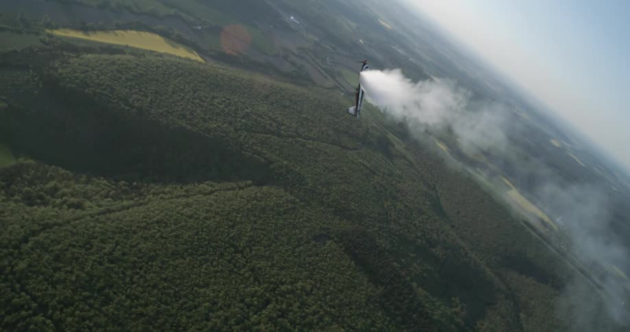 Aerial view of a small airplane with smoke coming out of it flying in the sky over treecovered mountains