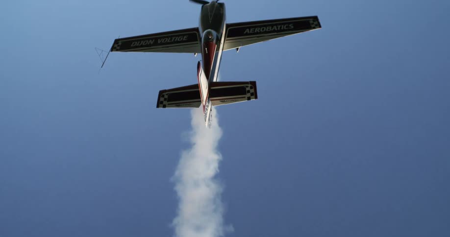 An airplane is flying in midair with white smoke trailing from the engine at midday