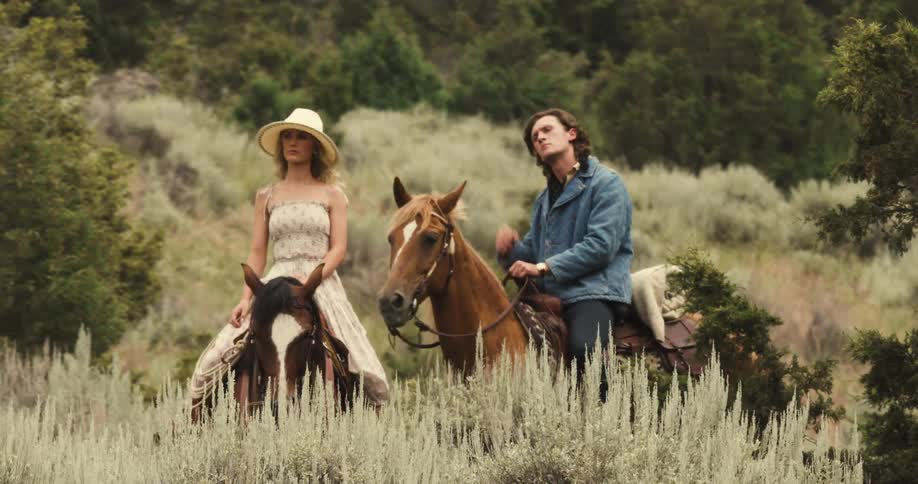 Man and woman riding a horse through a field in the mountains