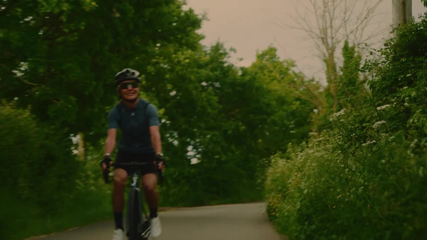 A cyclist riding a bicycle on a road surrounded by many trees and greenery