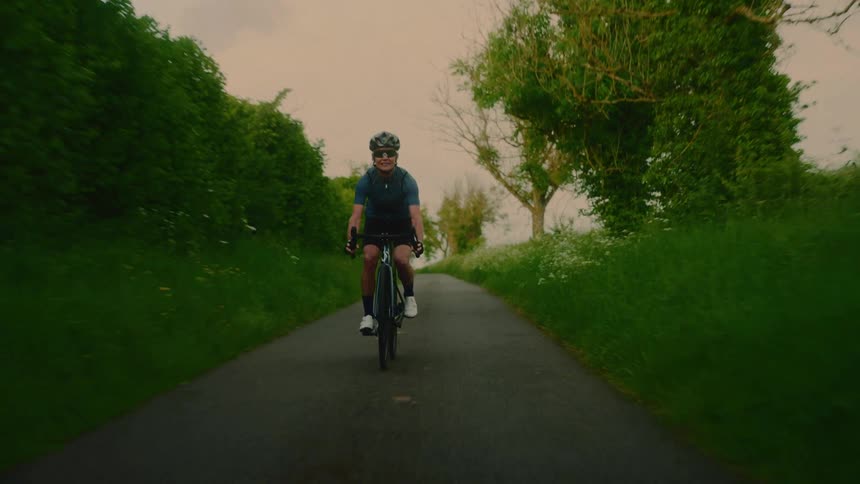 Woman wearing a helmet and sunglasses cycling along a wooded trail