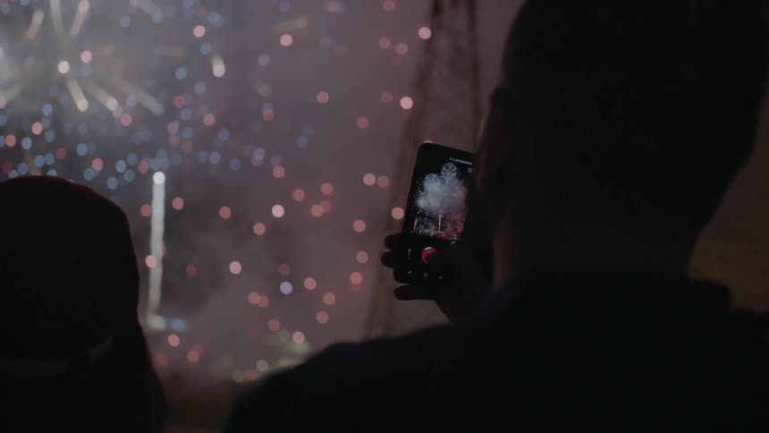 A man films fireworks that are exploding overhead