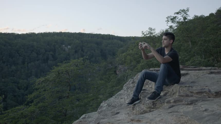 Man sits at the edge of a cliff and takes a picture