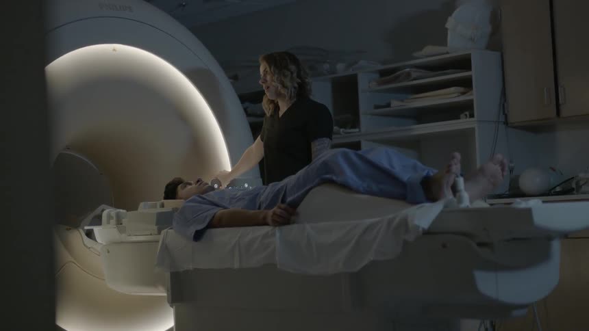 A woman is standing over a patient near an mri