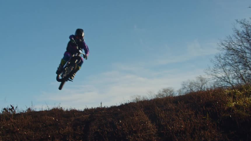 Motorcyclist launches off a dirt hill against a clear blue sky