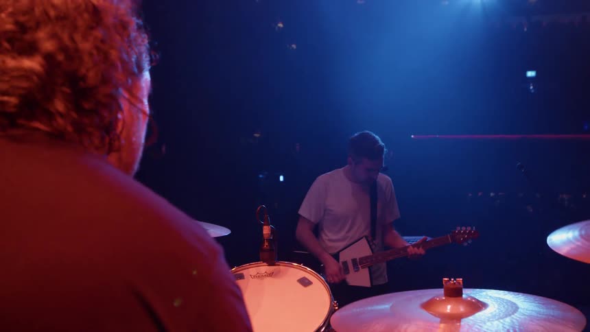 A guitarist performs on stage in front of a live audience viewed from behind a drummer