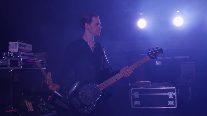 Man holding a guitar is hitting a drum with a stick on a stage