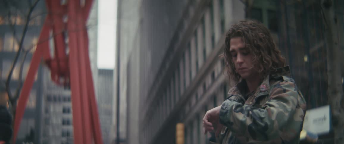 Man checks his wristwatch while standing on a busy street at dawn