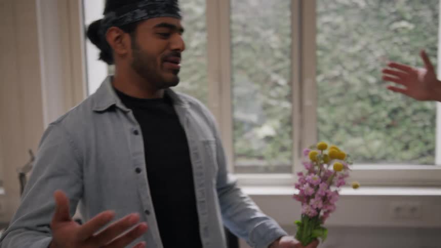 Two men hug warmly in an office one holding a bouquet of flowers