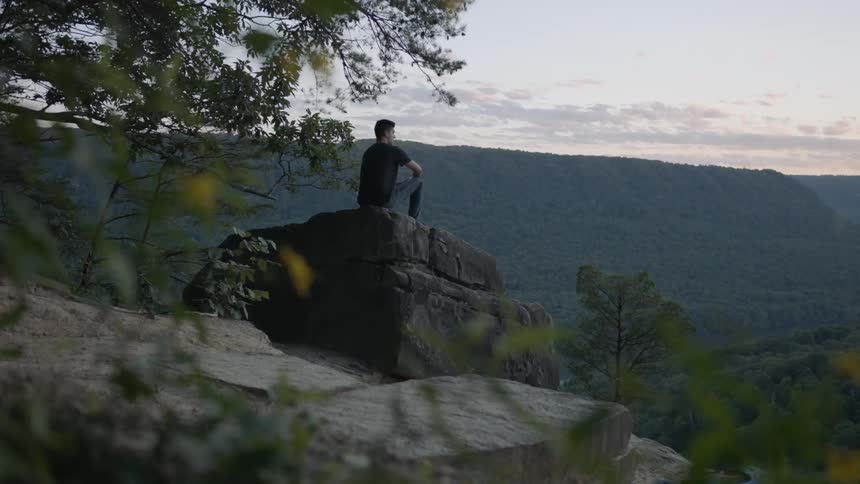 A man sits on a boulder near a cliff