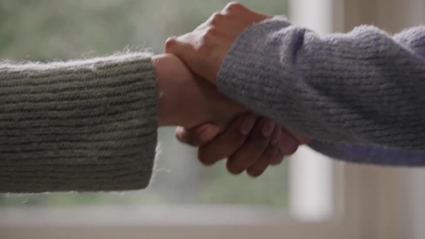 Two people are shaking hands both wearing longsleeved sweaters