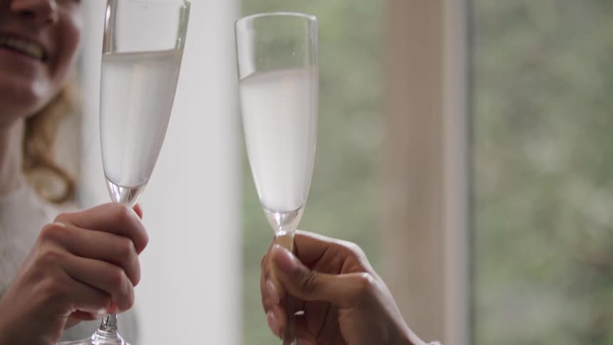 Close up of two women hitting their wine glasses together in celebration