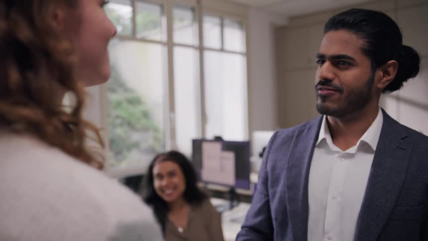 A woman walks into a large office where fellow coworkers congratulate her on an accomplishment