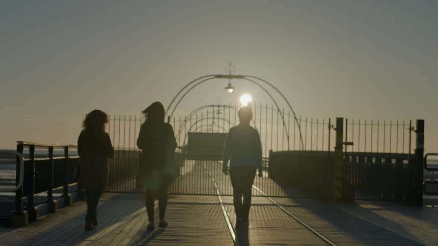 Three people walk along a pier