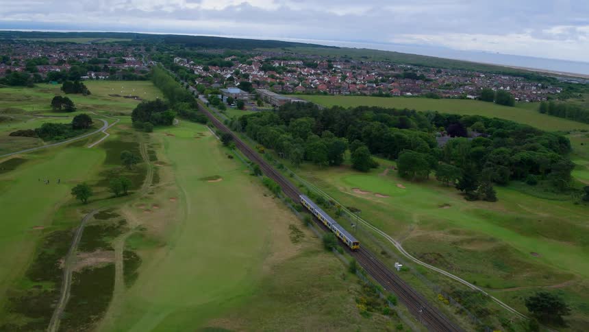 A train travels down a track next to green fields