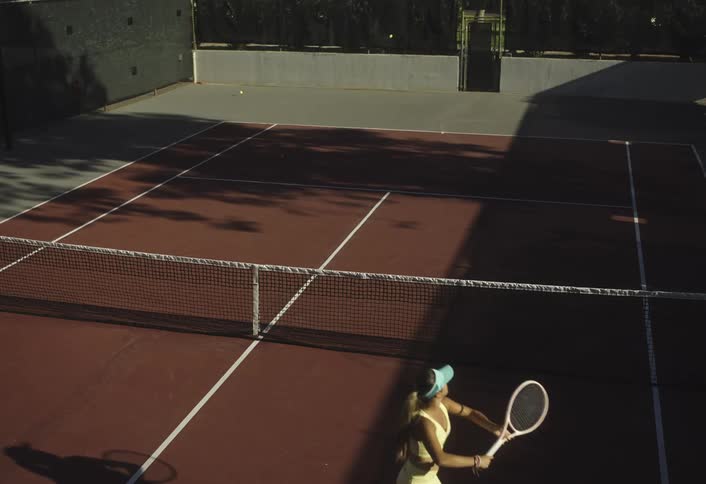 Female tennis player trains by smashing balls across the outdoor court during daytime