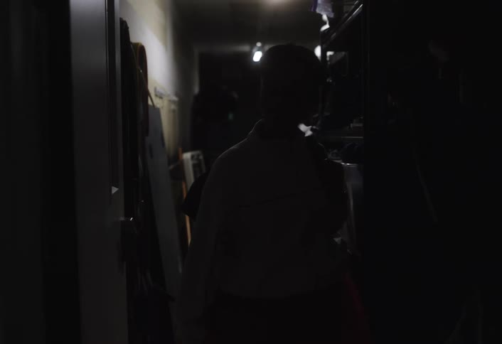 A woman walks down the hallway into a room and then turns on the light