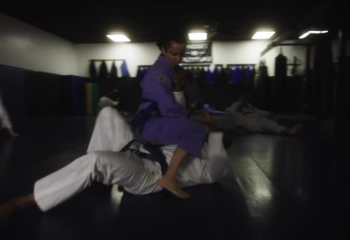Martial artists in white uniforms spar on a gym mat during a training session