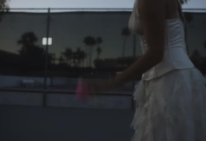 Lady in white dress bounces tennis ball at dawn on the tennis court
