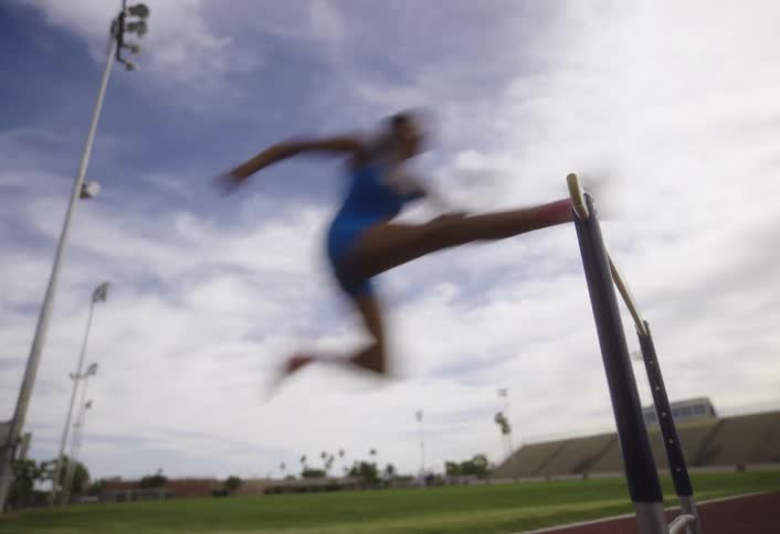 Lady jumps over a hurdle in the stadium at daytime
