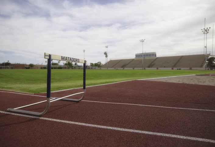 A female runner jumping over a hurdle on a track outdoors