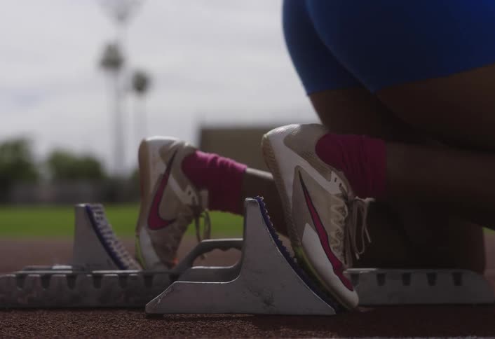 An athlete is in the starting blocks on a track ready to begin a race at midday
