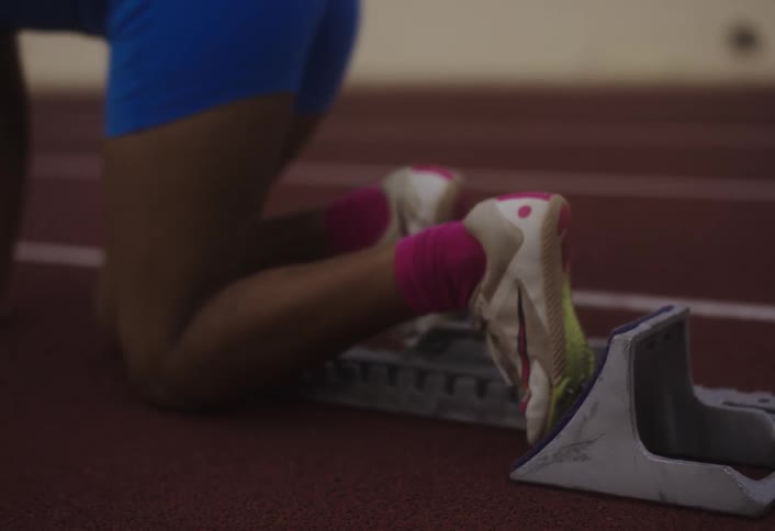A track runner sets into position and takes off sprinting on the track at midday