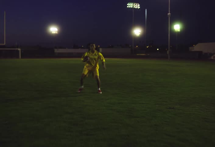 A woman running on a field in a stadium while holding an american football