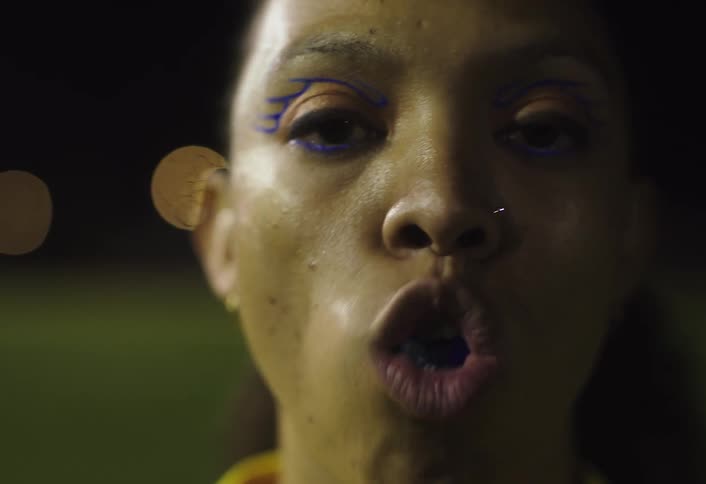 Close up of a black female footballer inserting a mouth guard while standing on a field at night
