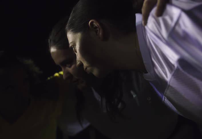 Female football players gather in a group hug during a timeout at night for a tactical discussion during a match