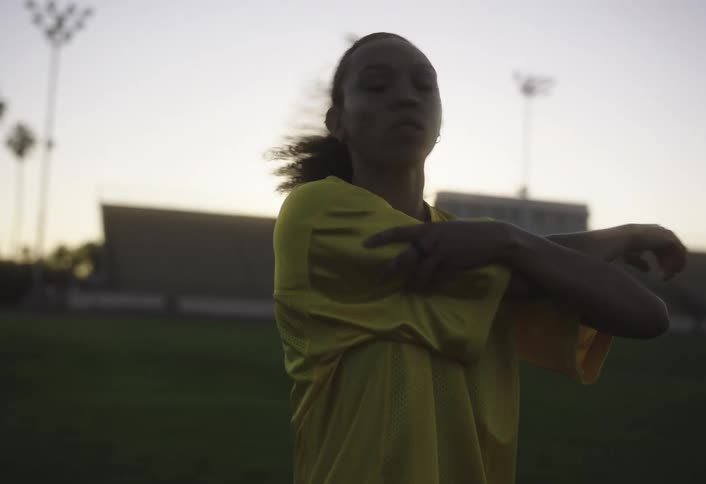 Woman in yellow tshirt on a soccer field stretching her arms