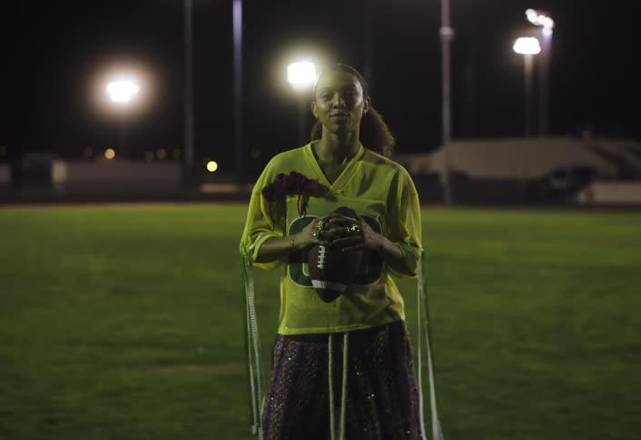 A woman standing on an american football field holding a football